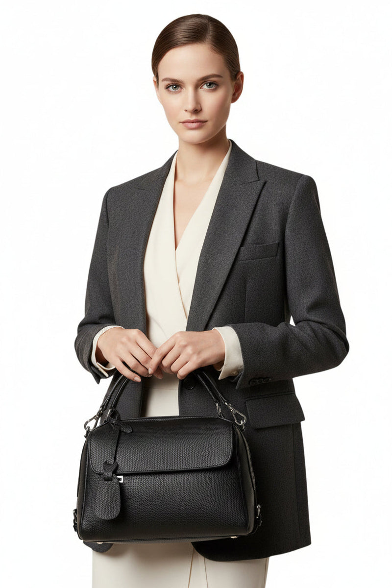 Season pestige black full-grain leather crossbody bag with a slouchy silhouette held by a model in a grey blazer.